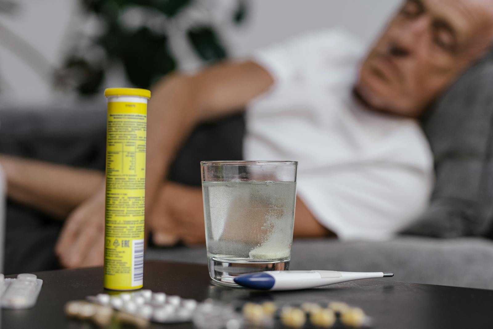An elderly man resting on a couch with medicine, illustrating recovery or illness.