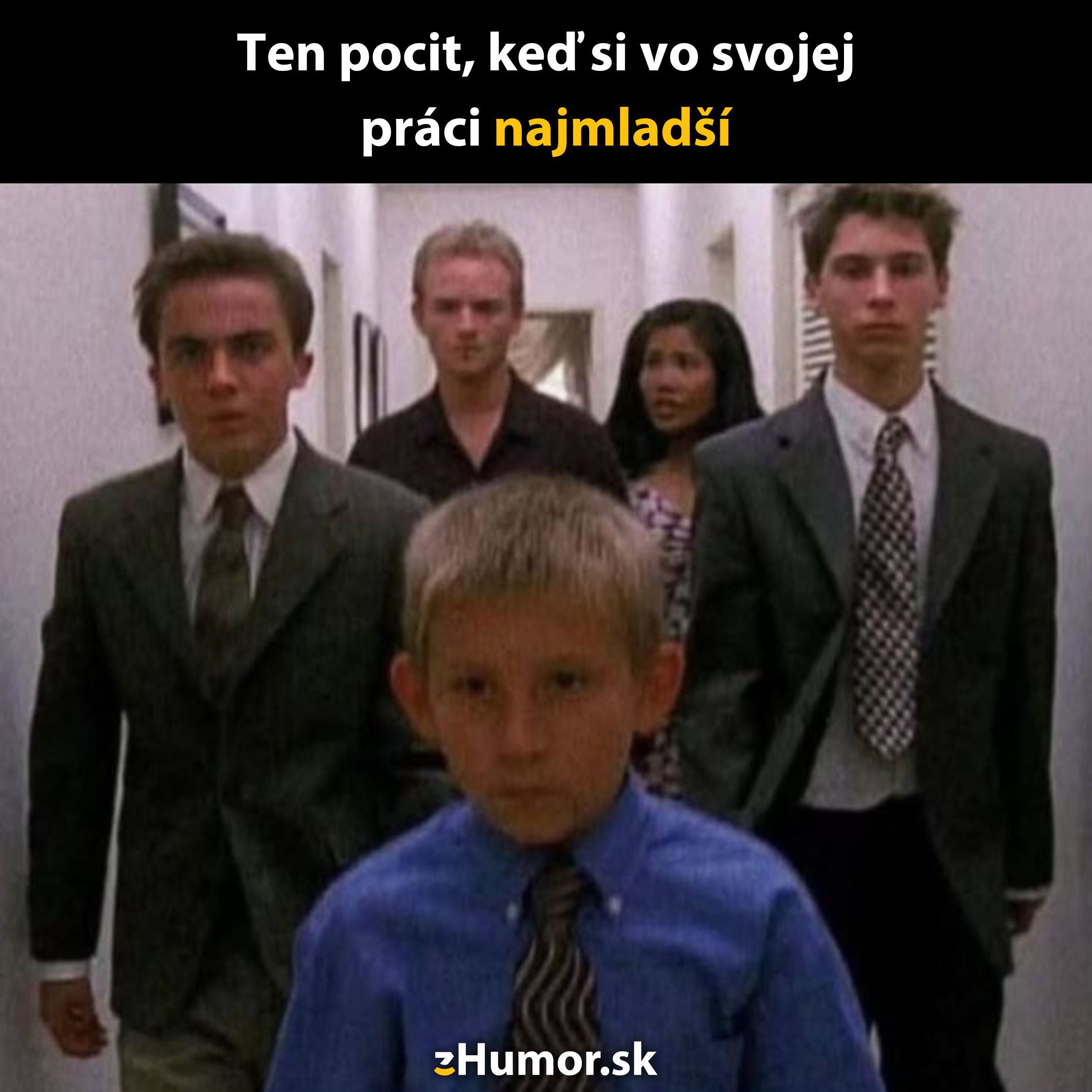 Malý chlapec v obleku kráča po chodbe, nasledovaný skupinou dospelých. Text: Ten pocit, keď si v práci najmladší.