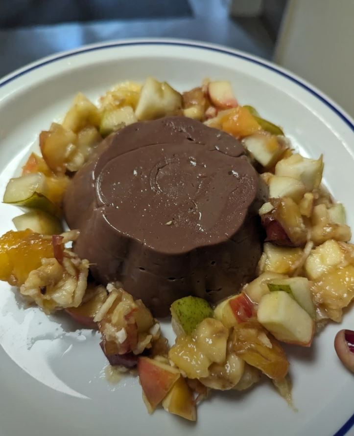 Čokoládový puding s čerstvým ovocným šalátom na bielom tanieri.