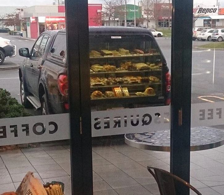 Auto s výkladom plným pečiva zaparkované pred kaviarňou s presklenými dverami.