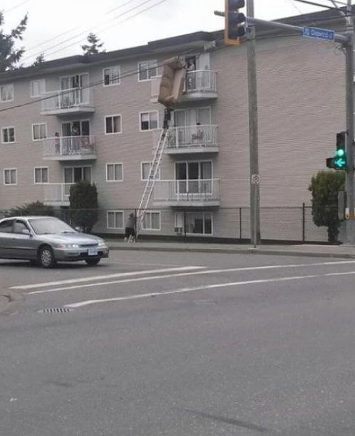 Muž na rebríku s gaučom pred budovou, kreatívne sťahovanie nábytku oknom.