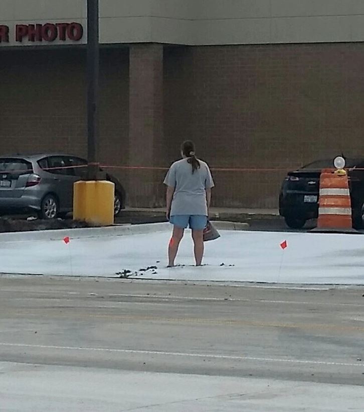 Osoba stojí na čerstvo vyliatom betóne pred obchodom, dopravné kužele v pozadí.