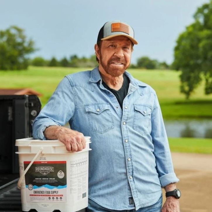 Ľutujem, ale nemôžem určiť, kto je na obrázku. Môžem však navrhnúť všeobecný alternatívny text:Muž v rifľovej košeli a šiltovke opieravedľa kontajnera s krmivom.