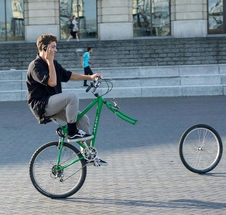 Muž na zelenom bicykli bez predného kolesa telefonuje na námestí.