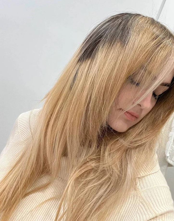 Žena s dlhými, blond vlasmi v béžovom svetri, sklonená hlava.