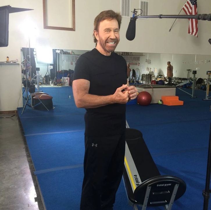 Osoba cvičí vo fitnes centre, usmieva sa pred kamerou s mikrofónom. V pozadí sú cvičebné pomôcky.