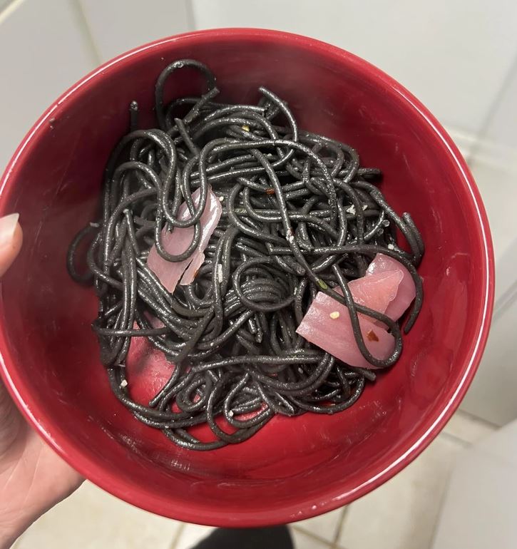 Čierne špagety so surovým rybím mäsom v červenej miske, detail zhora.