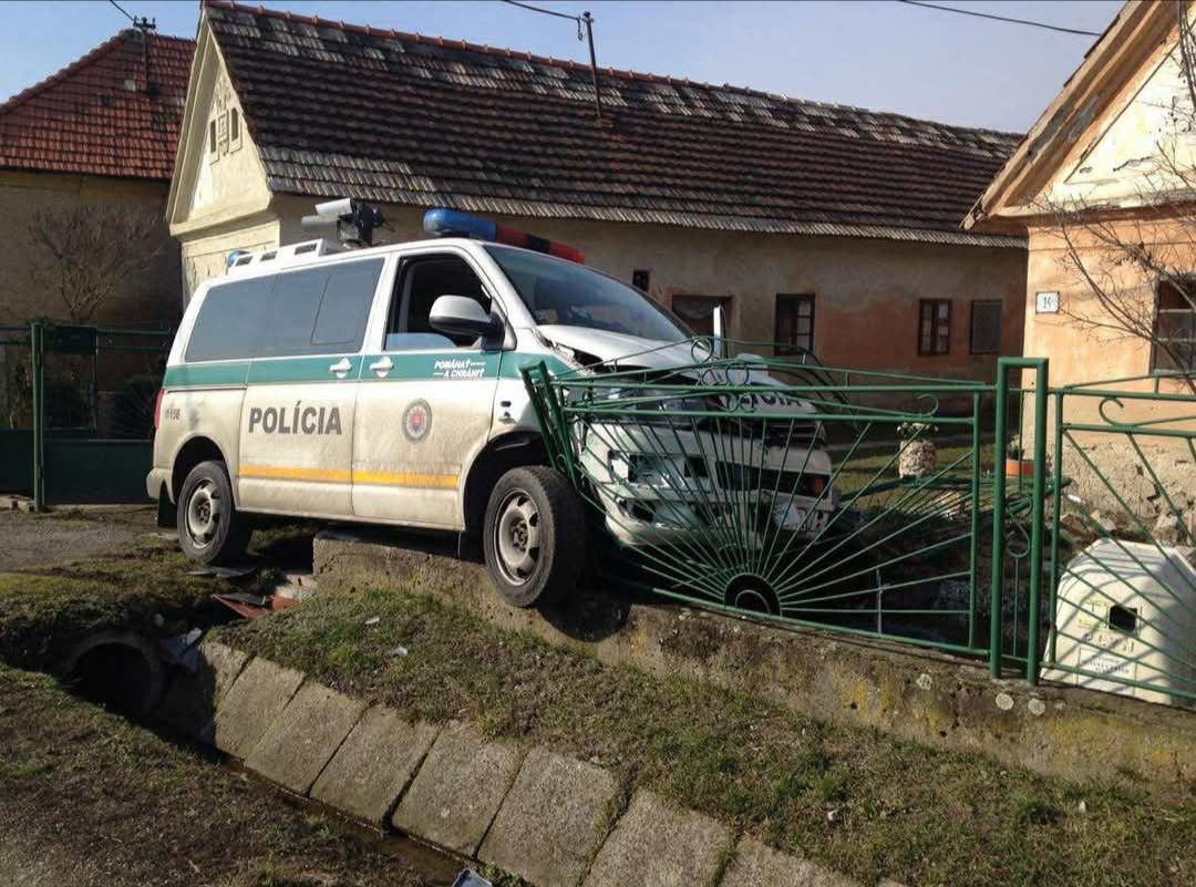 Policajné auto narazilo do plotu v dedinskom prostredí, poškodené brána zelená.