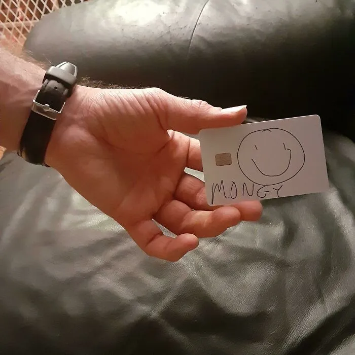 Ruka držiaca kreslenú kreditnú kartu s úsmevom a nápisom MONEY na koženom pozadí.