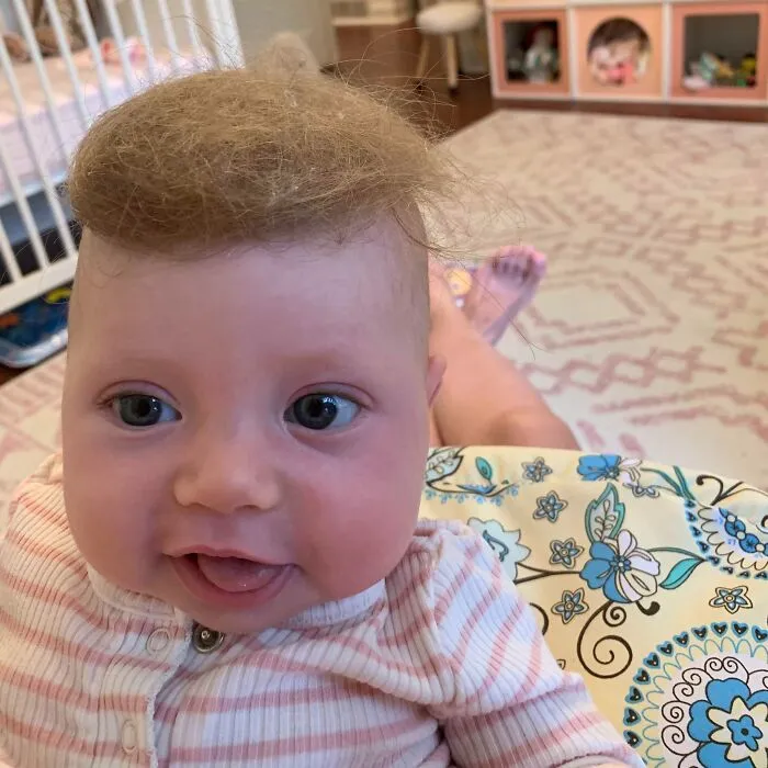 Dieťa s roztomilým účesom, sedí v jasličkách, oblečené v pruhovanom pyžamku, s úsmevom na tvári.