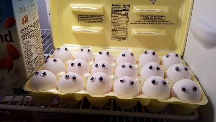 Vajcia s nalepenými plastovými očami v kartóne v chladničke, vytvárajú zábavnú a hravú scénu.