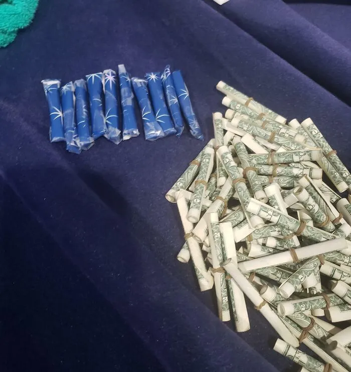 Odkryté modré balíčky a zvinuté dolárové bankovky na tmavom povrchu.