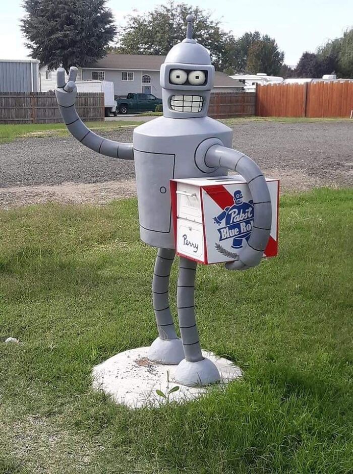 Robot so zdvihnutým V-znakom drží balenie plechoviek piva na záhrade.