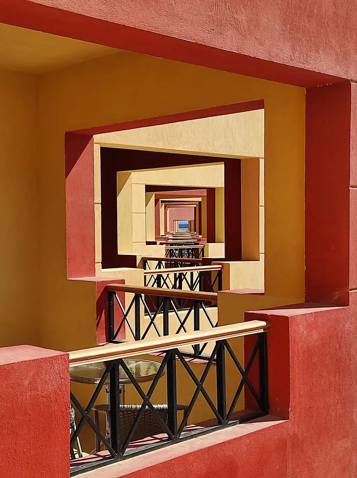 Moderná architektúra: pohľad cez geometrické červené a žlté rámy na slnkom zaliatu terasu.