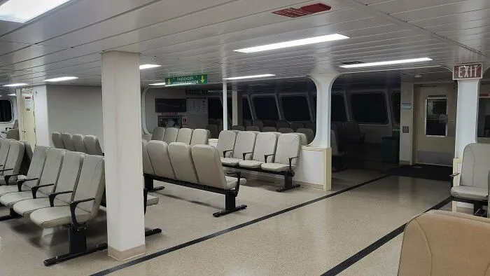 Prázdna čakáreň s radmi sediacich miest, bielymi stenami a smerovými znakmi k východu, dobre osvetlená.