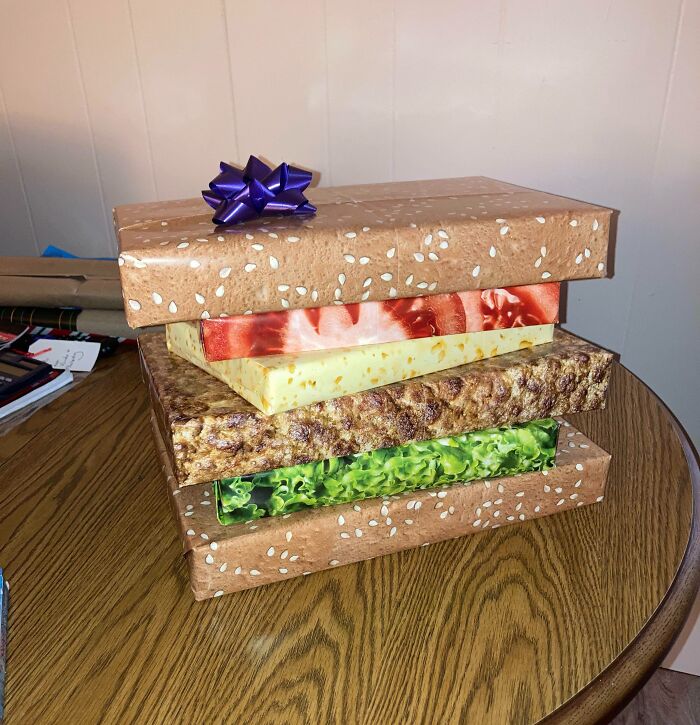 Krabice zabalené ako hamburger s rôznymi polevami na stole, ozdobené fialovou mašľou.