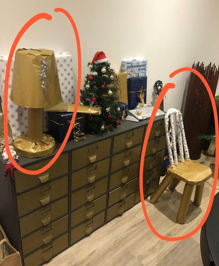 Vianočná výzdoba: komoda s darčekmi, ozdobený stromček, stolička a lampa zabalené do baliaceho papiera.