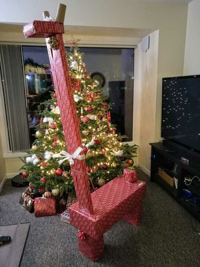 Vianočný stromček s darčekmi, zahalené vianočné prekvapenie v tvare žirafy vedľa televízie.