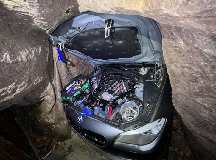 BMW s otvorenou kapotou v provizórnej opravovni, motor obklopený nástrojmi.