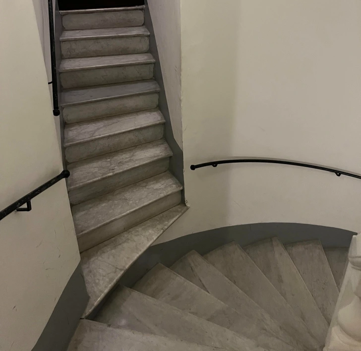 Schodisko s ostrým rohom, s mramorovými schodmi a čiernym zábradlím, pohľad zhora.