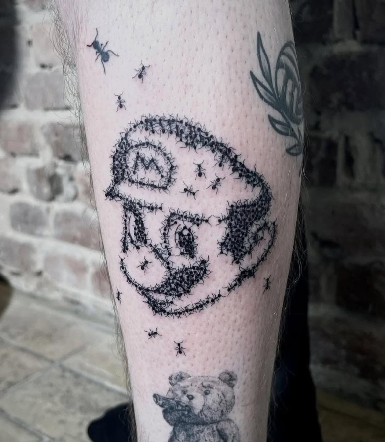Tetovanie na nohe znázorňujúce postavu vytvorenú z mravcov, s motívom plyšového medveďa pod ňou.