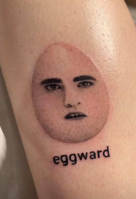 Tetovanie tváre na vajci s textom eggward na predlaktí.