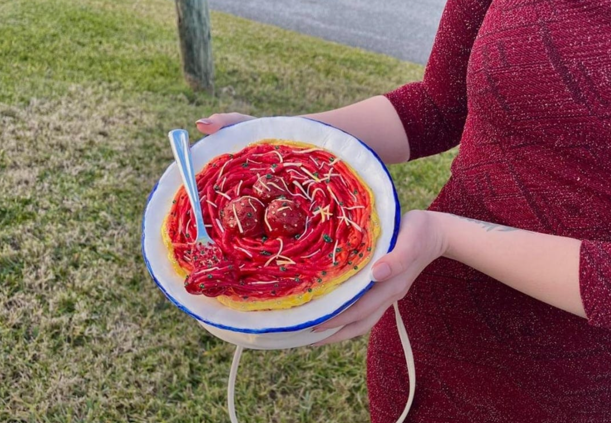 Osoba držiaca tanier s pastou, ktorý vyzerá ako špagety s červenou omáčkou a guľkami, v exteriéri.