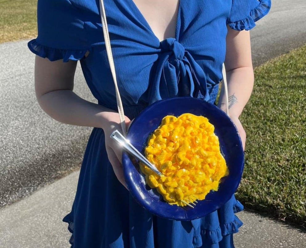 Osoba v modrých šatách držiaca tanier žiarivo žltého jedla na dvore.