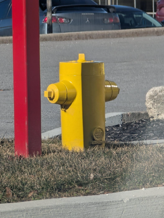 Žltý hydrant vedľa červenej konštrukcie na parkovisku, detailný pohľad, slnečný deň.