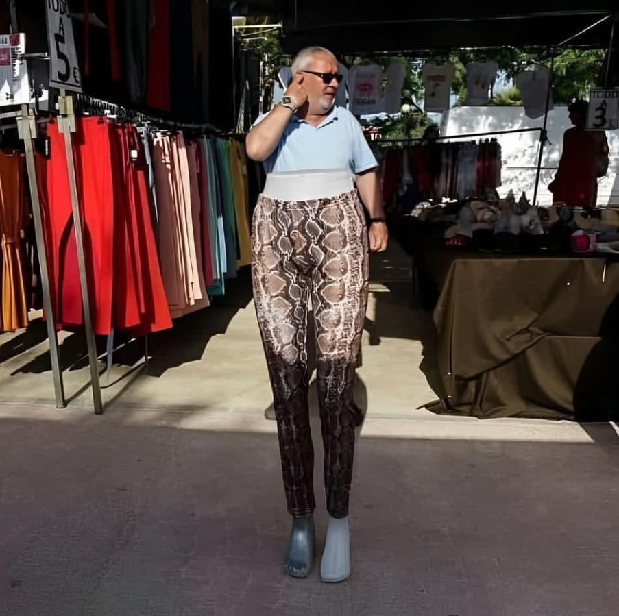 Muž srandovne pózuje s nohavicami na figuríne na vonkajšom mestskom trhu plnom oblečenia.