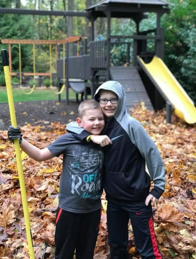 Dvaja chlapci sa hrajú pri detskom ihrisku s lístím a metlou v jesennom lese.