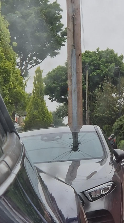 Auto s rozbitým čelným sklom po náraze do stĺpa, ulica obklopená stromami.