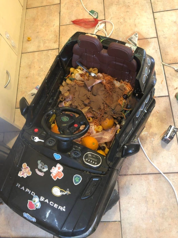 Detské elektrické autíčko plné odpadu a ovocia, neporiadok na podlahe v kuchyni.