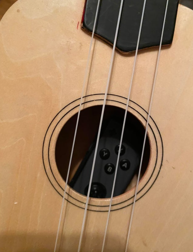 Ovládač hernej konzoly zasunutý vo vnútri ukulele, detailný pohľad na struny a telo nástroja.