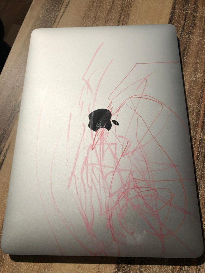 Strieborný notebook s červenými čmáranicami na zadnej strane, položený na drevenom stole.