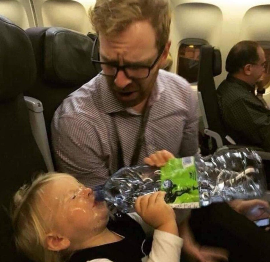 Otec a dieťa v lietadle, dieťa sa snaží piť vodu z fľaše a zaprskalo ju okolo seba.