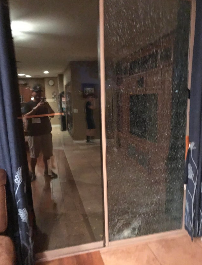 Muž fotí odraz cez popraskané sklenené dvere uprostred osvetlenej miestnosti.