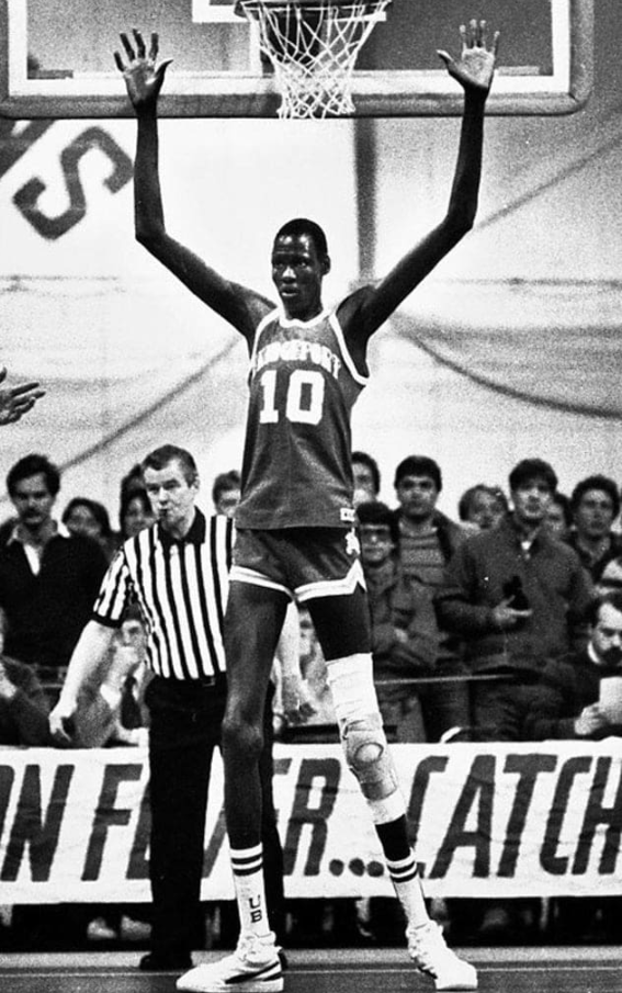 Basketbalista v drese s číslom 10 s rukami zdvihnutými nad hlavou počas zápasu, čiernobiela fotografia.