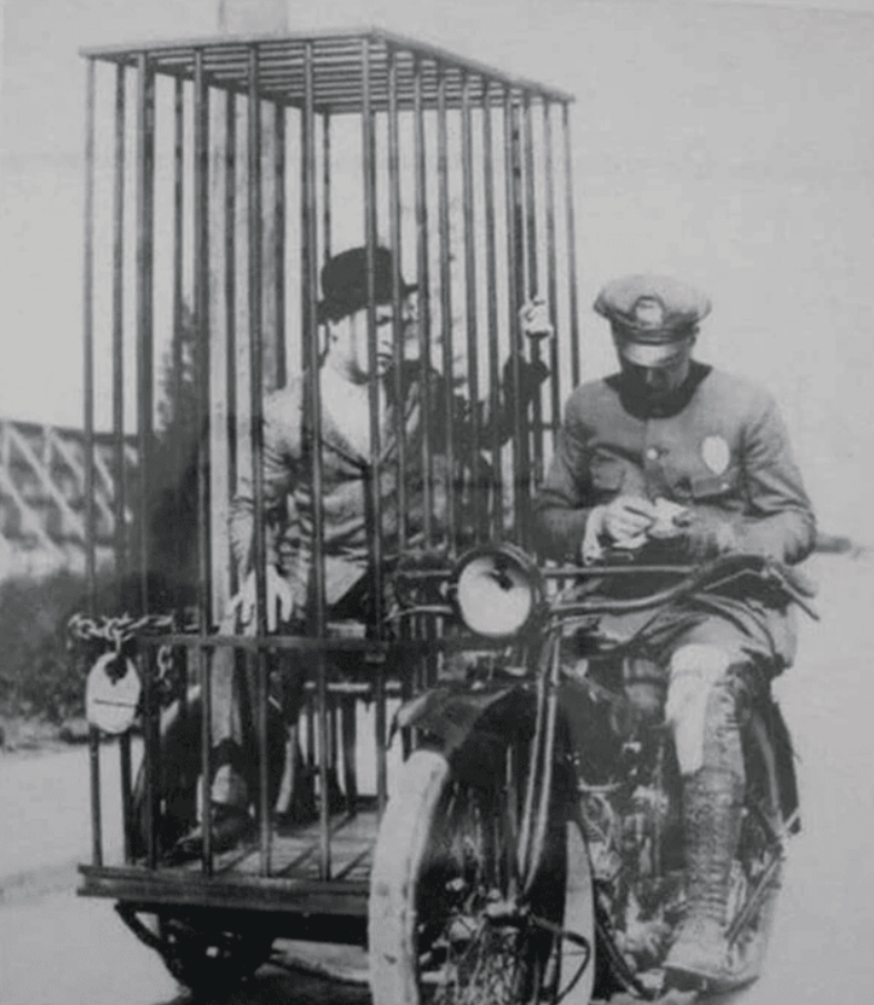 Historický motocykel s klietkou na prepravu väzňov, policajt píše poznámky. Vintage bezpečnosť na cestách.