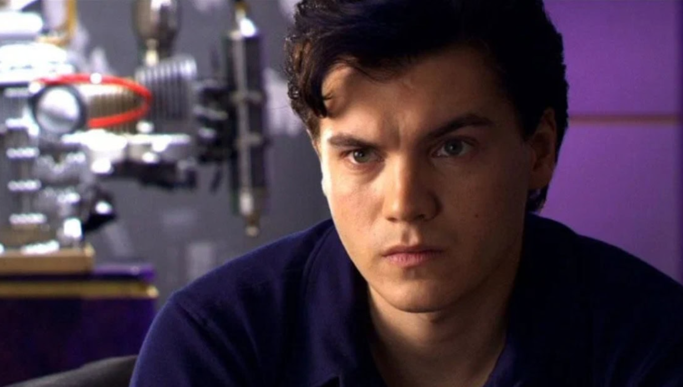 Osoba so zamysleným pohľadom na modernom pozadí, technické zariadenie vľavo rozmazané.