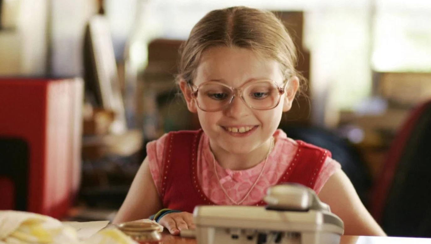 Dievča s okuliarmi sa usmieva pri pohľade na starú kameru v útulnej miestnosti.