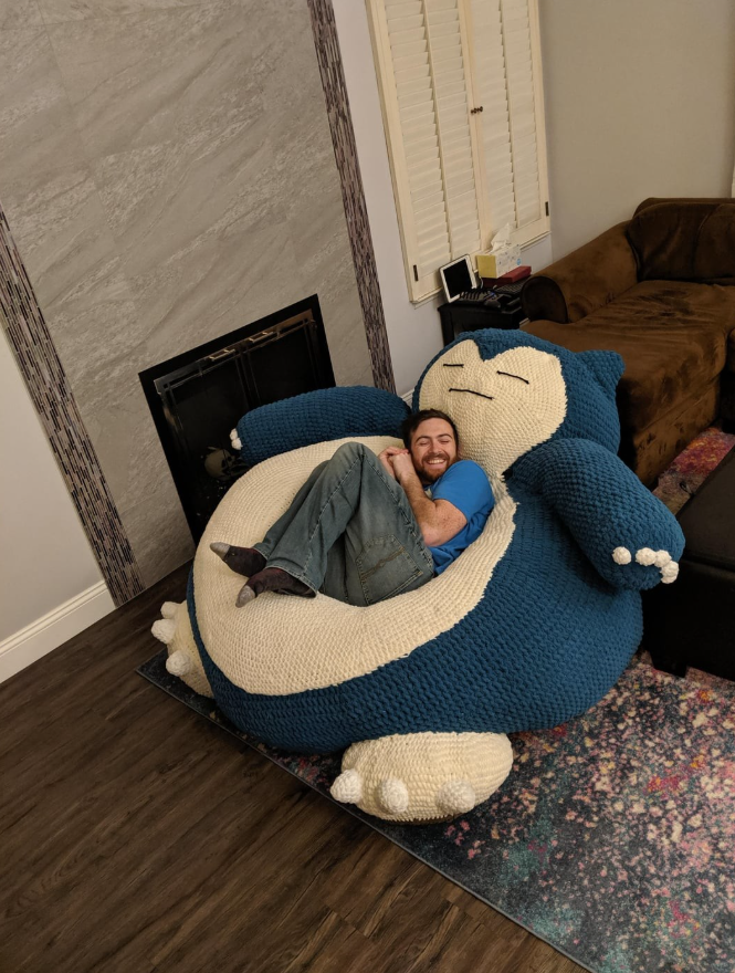 Osoba leží na veľkej pletenej hračke v obývačke, vyzerá pohodlne a spokojne.