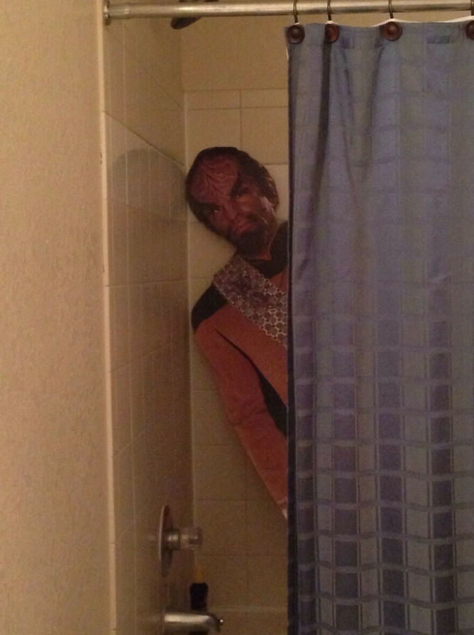 Klingon kartónová postava v kúte sprchového kúta za modrým závesom.
