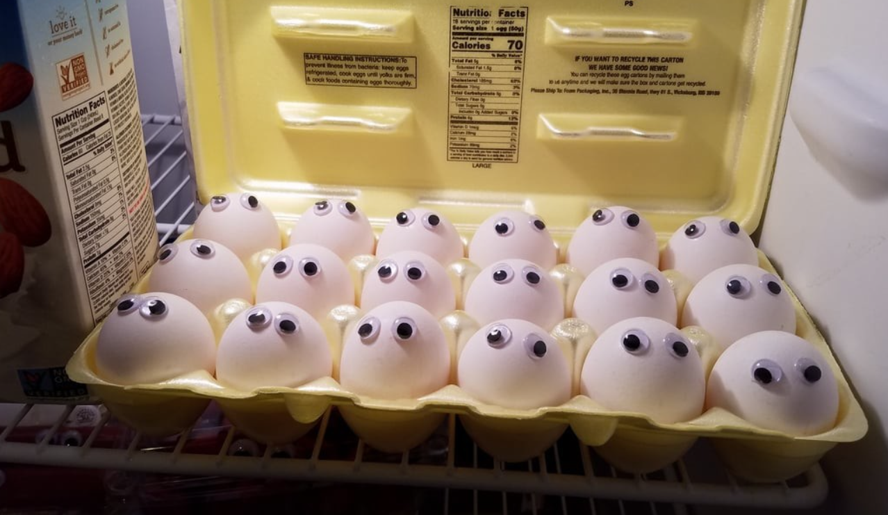 Kartón vajec s nalepenými očami v chladničke vytvára zábavnú a kreatívnu scénu.