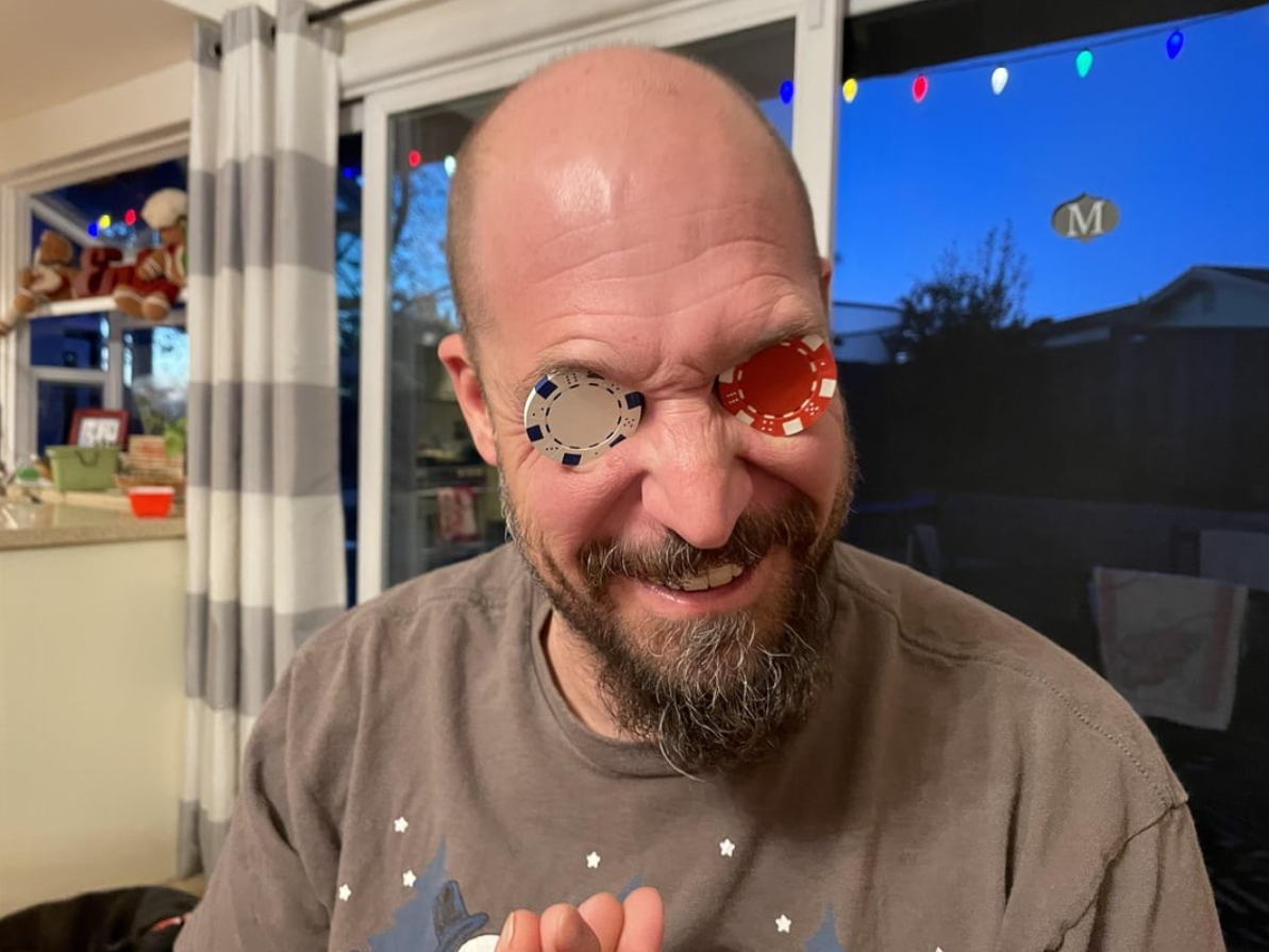 Muž vtipne drží pokerové žetóny pred očami v interiéri, zdobenom vianočnými svetielkami.