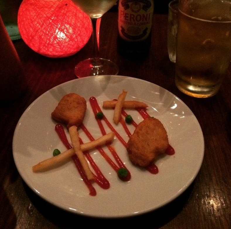 Elegantné jedlo s nugetkami, hranolkami a hráškom na tanieri s pivom a sviečkou v pozadí.