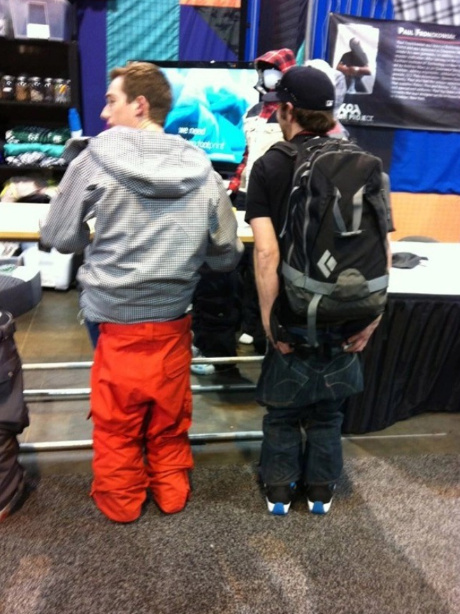 Dvaja muži v športovom oblečení stoja chrbtom na výstave outdoorových produktov.