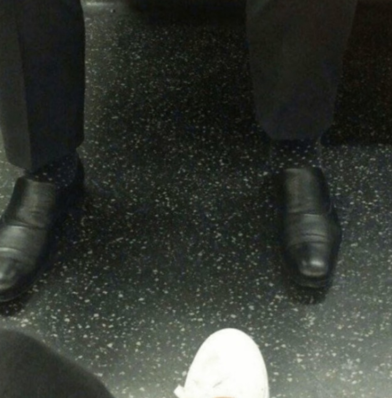 Čierne elegantné topánky a bodkované ponožky na tmavej podlahe v kombinácii s bielou športovou obuvou.