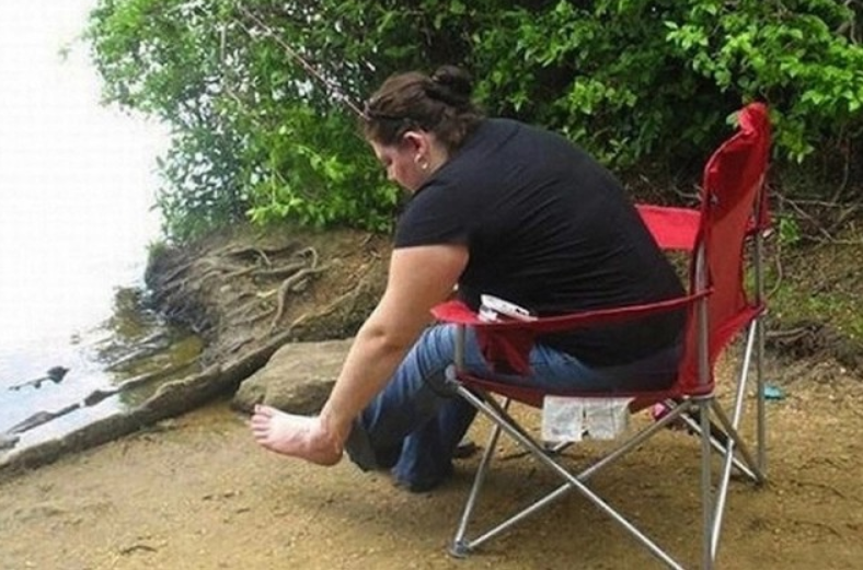 Osoba sedí pri vode na červenej stoličke, venčuje sa svojim nohám v prírodnom prostredí.