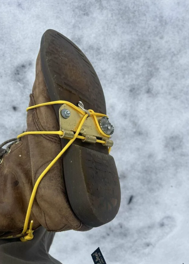 Topánka s protisklzovým uchytením na ľad, domácky pripevnená na snehu pomocou žltých popruhov a skrutiek.